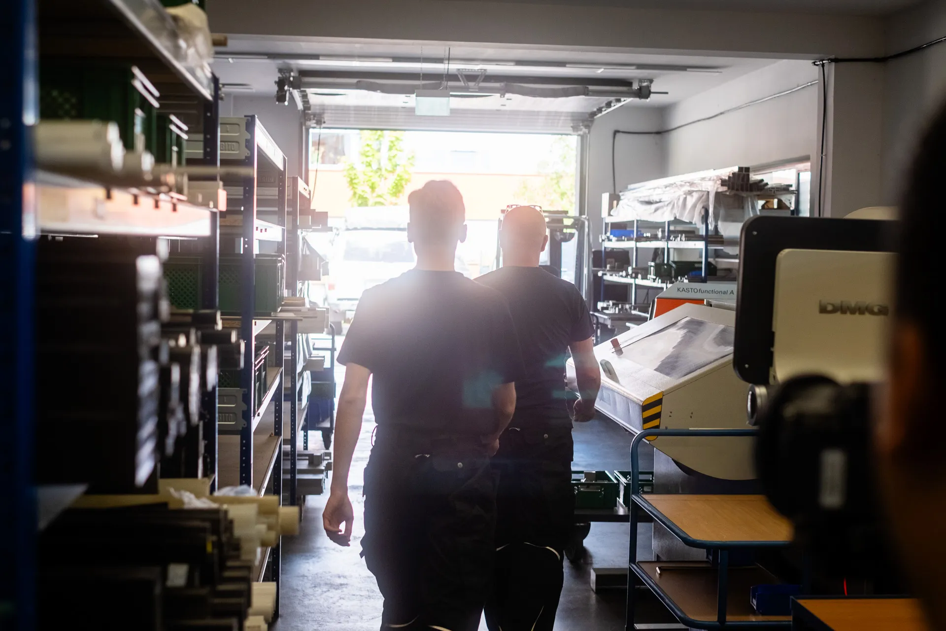 Mitarbeitende im Fertigungsbereich zwischen Regalen, Materialkisten und Maschinen